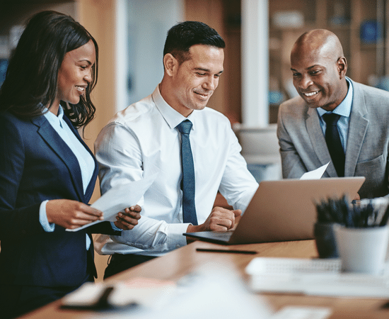 Three people are looking at a laptop in an office.