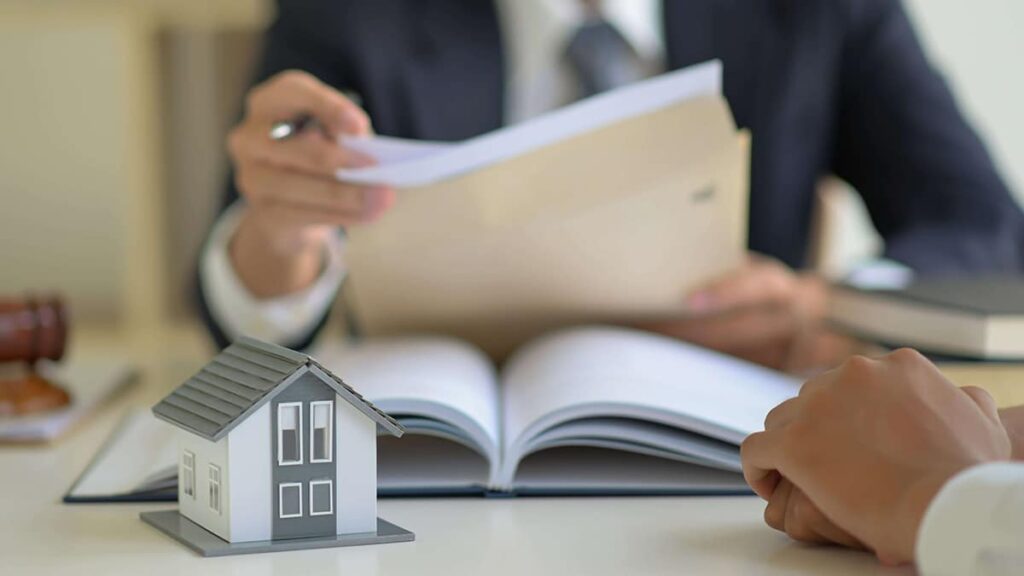 A person sitting at a table with an open book and model house.